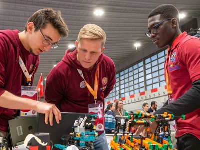 Drei Jugendliche begutachten interessiert einen Roboter Prototyp