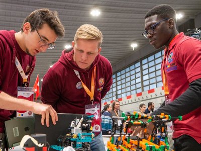 Drei Jugendliche begutachten interessiert einen Roboter Prototyp