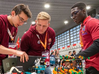 Drei Jugendliche begutachten interessiert einen Roboter Prototyp