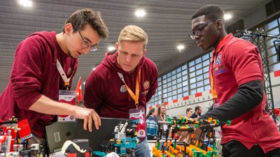 Drei Jugendliche begutachten interessiert einen Roboter Prototyp