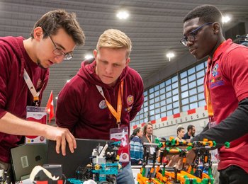 Drei Jugendliche begutachten interessiert einen Roboter Prototyp