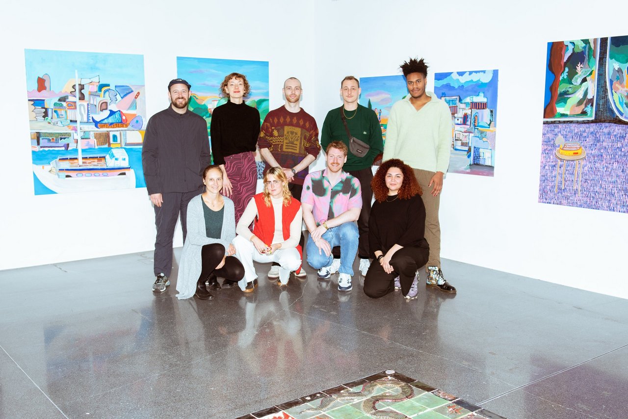 Neun ausgewählte Kunstschaffende stehen vor einer Wand mit Kunstwerken