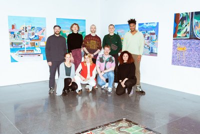 Neun ausgewählte Kunstschaffende stehen vor einer Wand mit Kunstwerken