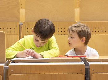 Zwei Kinder sitzen im Hörsaal und machen Notizen