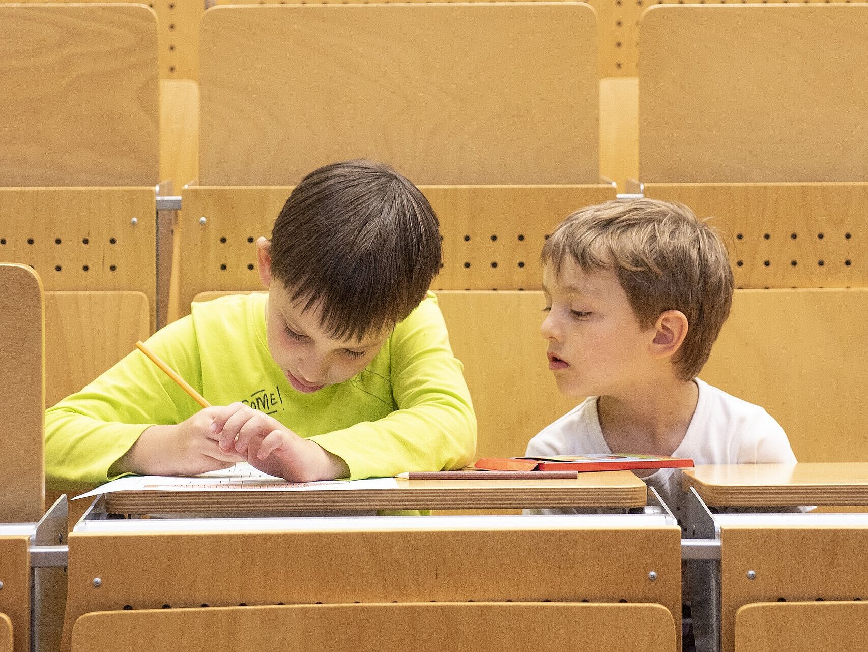 Zwei Kinder sitzen im Hörsaal und machen Notizen