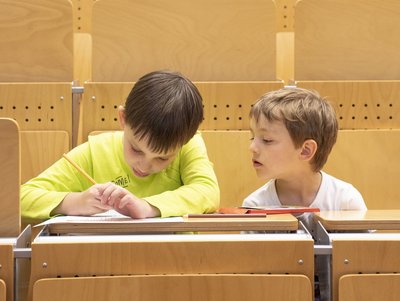 Zwei Kinder sitzen im Hörsaal und machen Notizen
