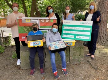 Kinder und Mitarbeitende der Gilden Grundschule halten Robotermaterial und einen Spendencheck