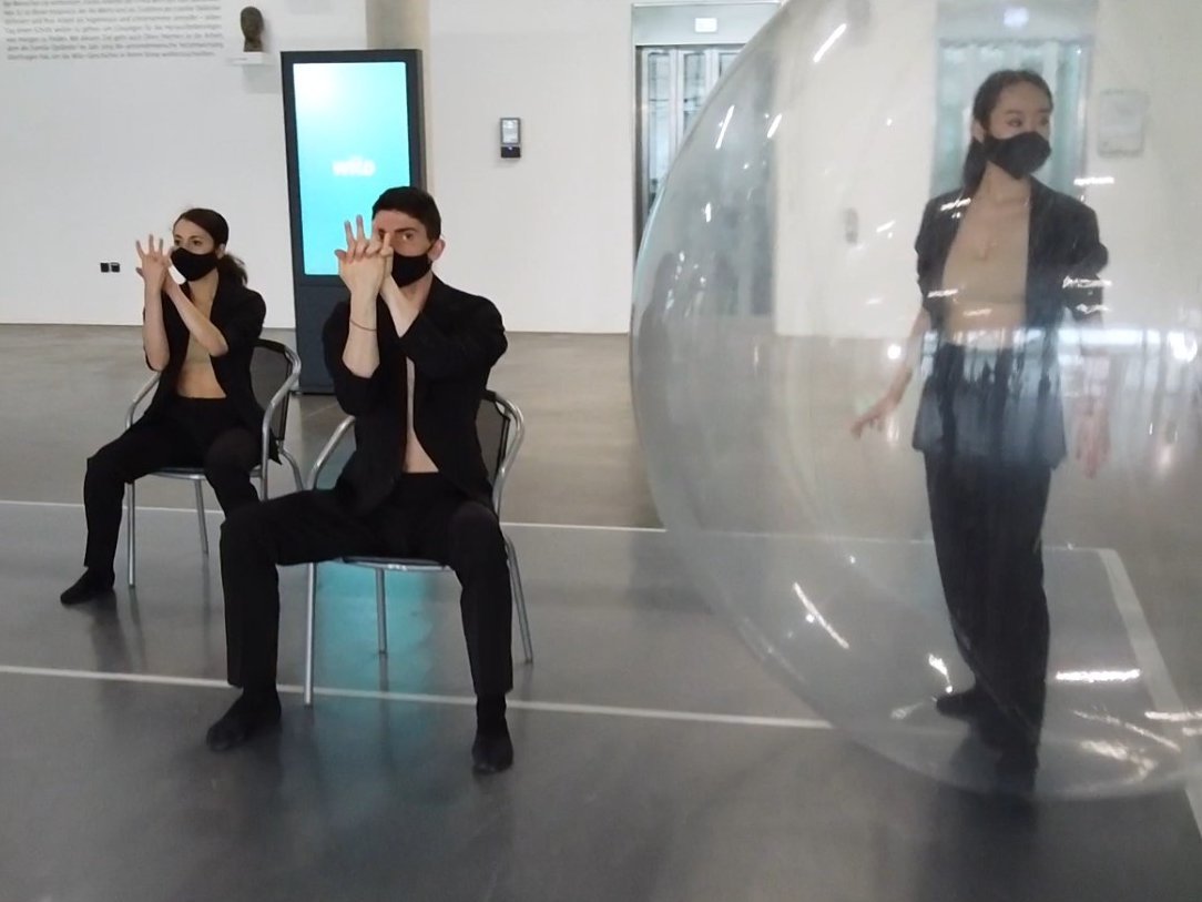 Künstlerinnen und Künstler des NRW Junior Balletts am Theater Dortmund, zwei Personen auf einem Stuhl, eine Person in einem transparenten Ballon