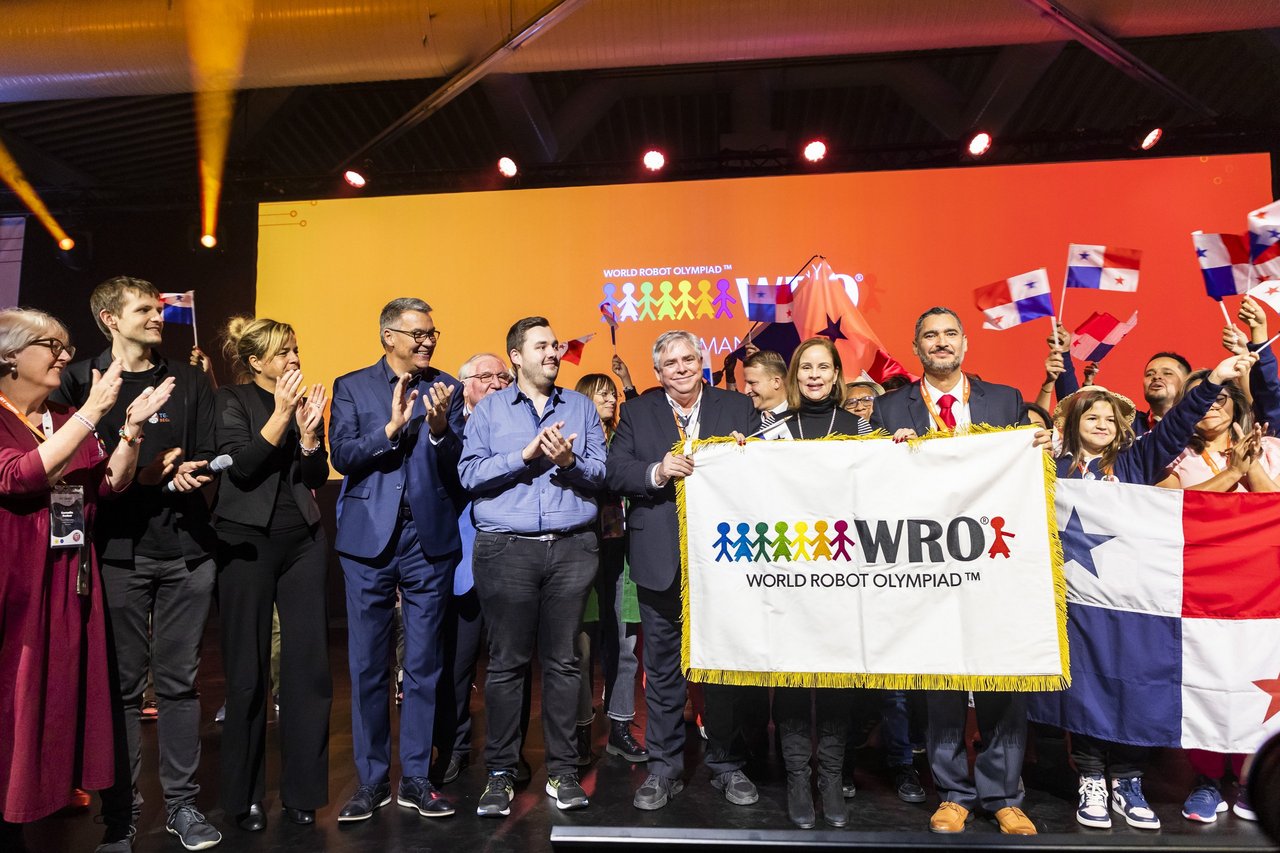 Auf einer Bühne stehen mehrere klatschende Menschen zur Eröffnungsfeier der World Robotic Olympiade