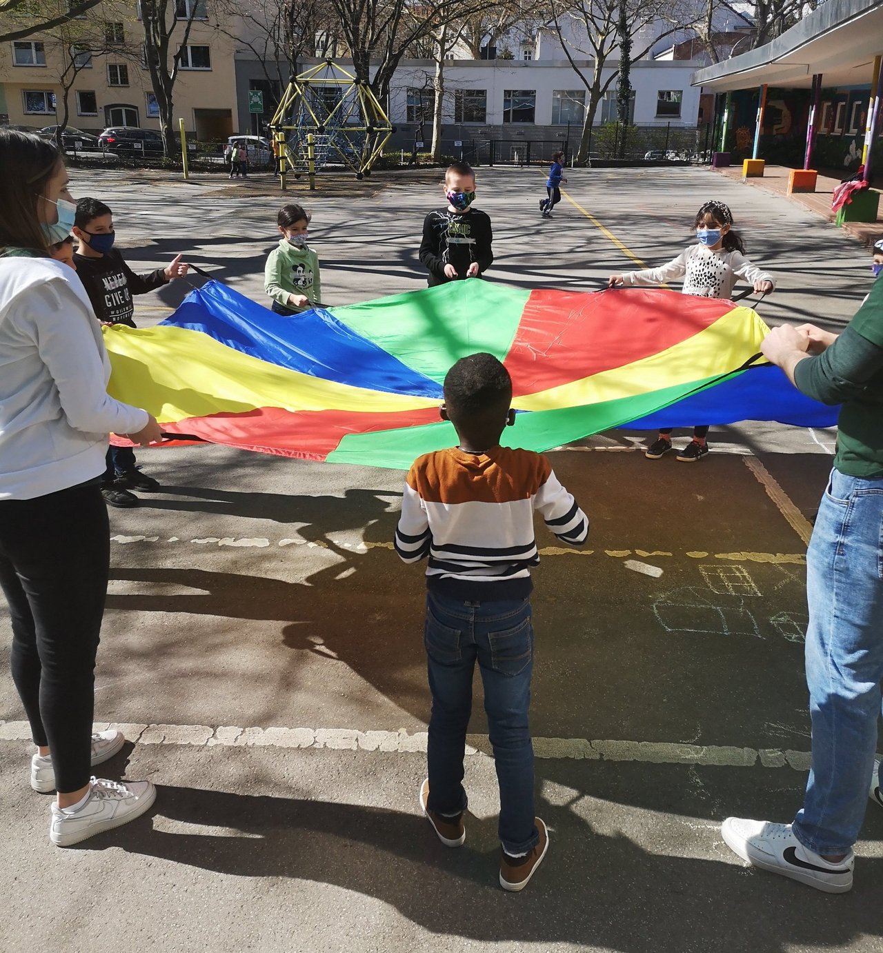 Kinder und Mitarbeitende spannen ein buntes Tuch auf einem Hof