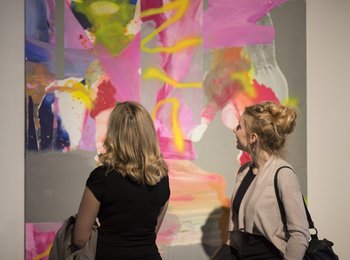 Zwei Frauen stehen vor einem großflächigen abstrakten Kunstwerk