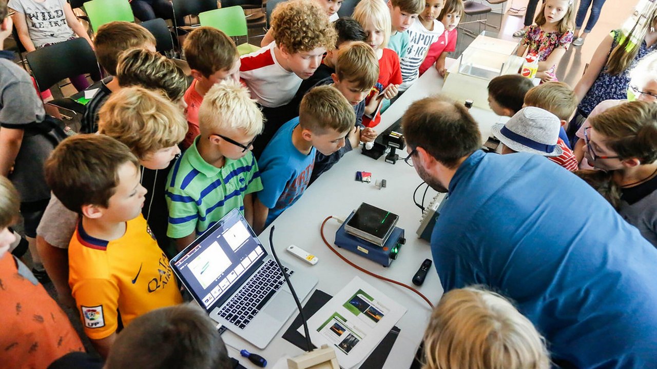 Mehrere Kinder stehen um einen Tisch, auf dem ein Experiment aufgebaut ist