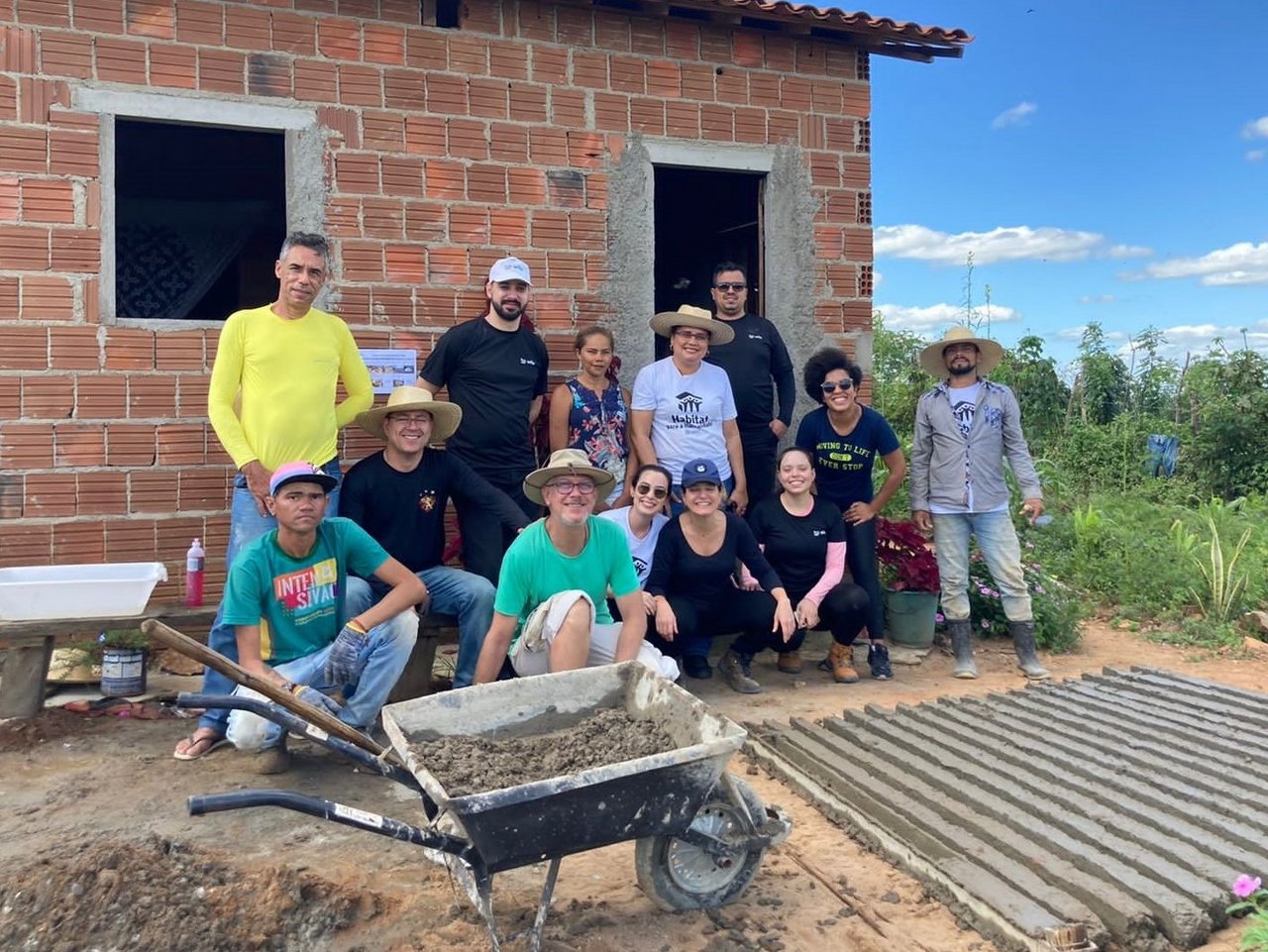 Freiwillige Helfer von Wilo Brasil stehen mit einer Familie vor dem Rohbau ihres Hauses, eine Schubkarre mit Beton im Vordergrund